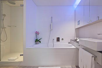Badezimmer mit Badewanne, Dusche und WC, Fernsehbildschirm im Spiegelschrank